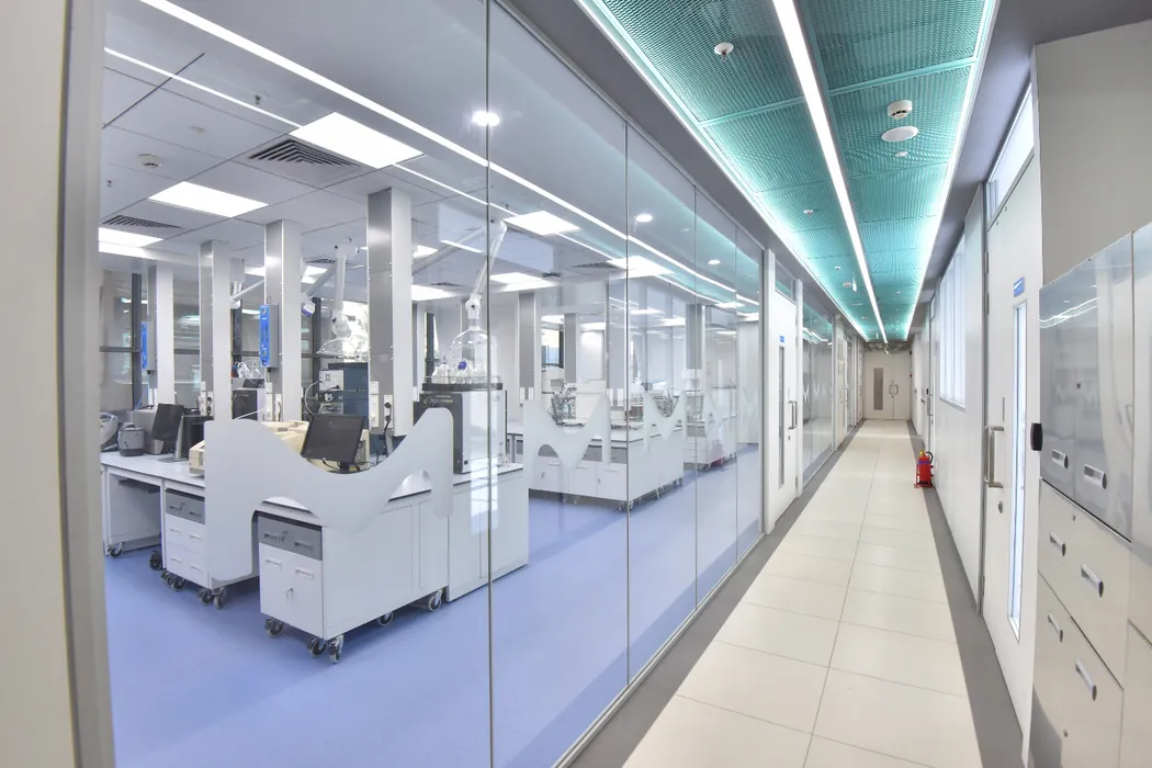 Clean laboratory corridor with teal perforated ceiling and glass walls