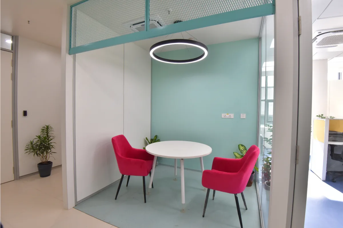 Teal breakout nook with magenta chairs, round table and ring pendant light