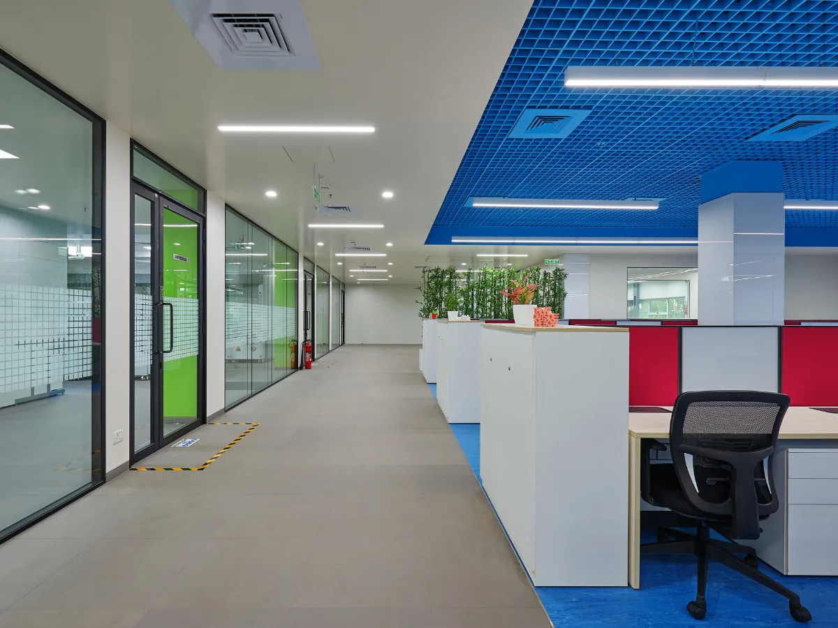Corridor with glass-walled labs on left and workstations under blue grid ceiling on right