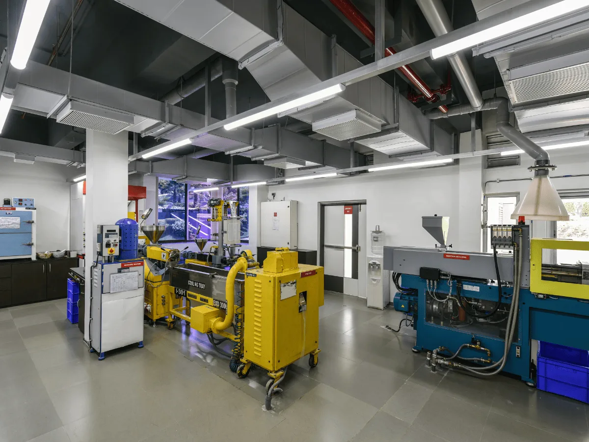 Plastic lab with yellow pelletizer, blue injection moulder and canopy hoods