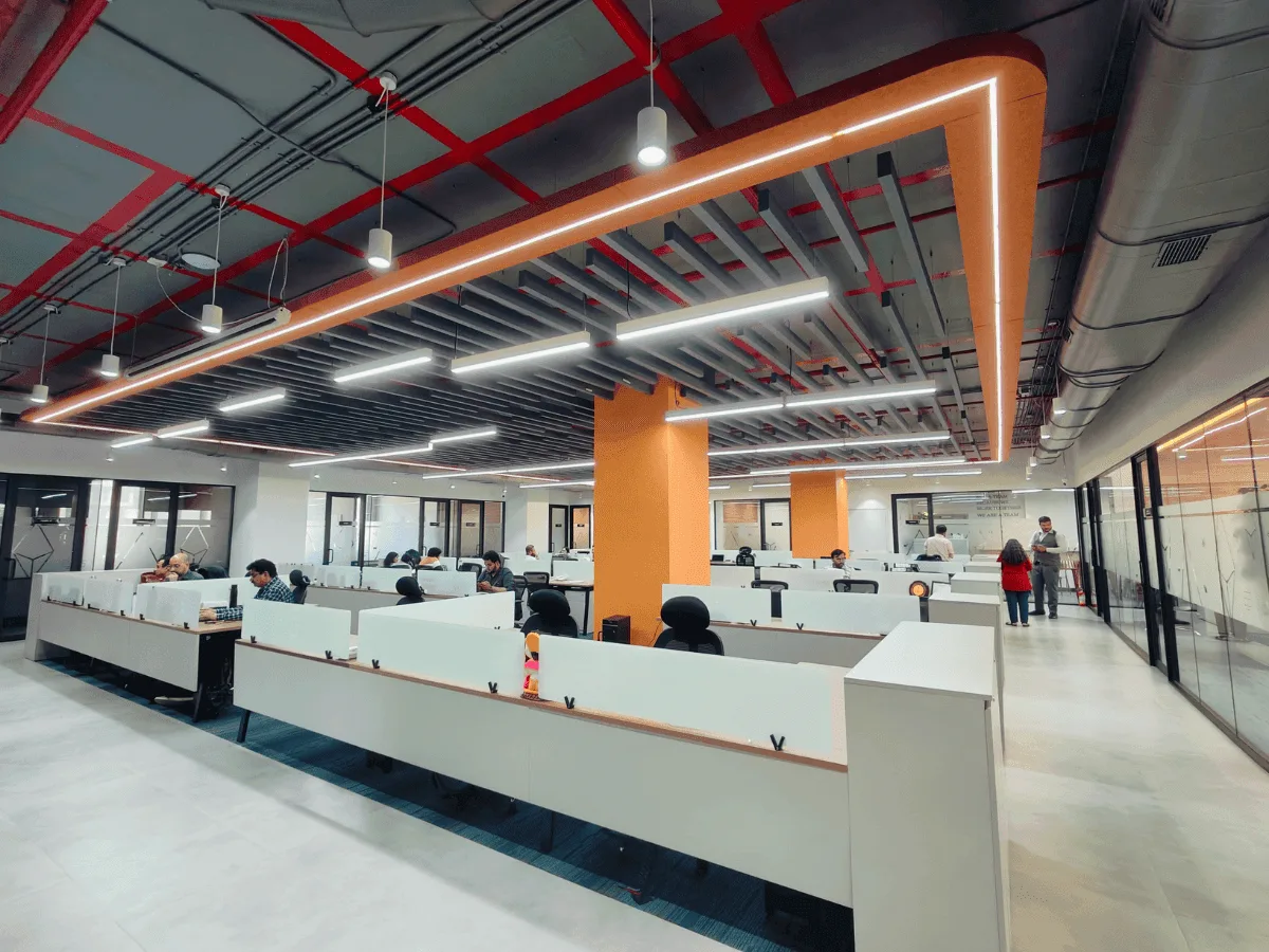 Open-plan workstations with orange columns and exposed ceiling baffle lights