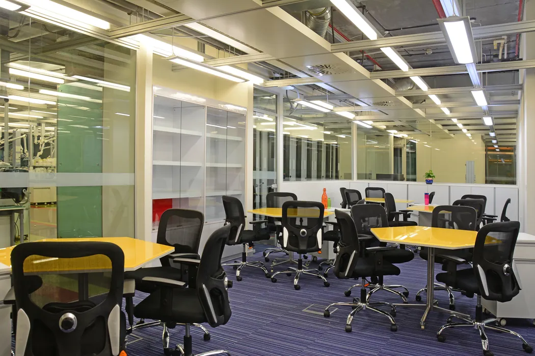 Collaborative workspace with yellow tables, mesh chairs and display shelving